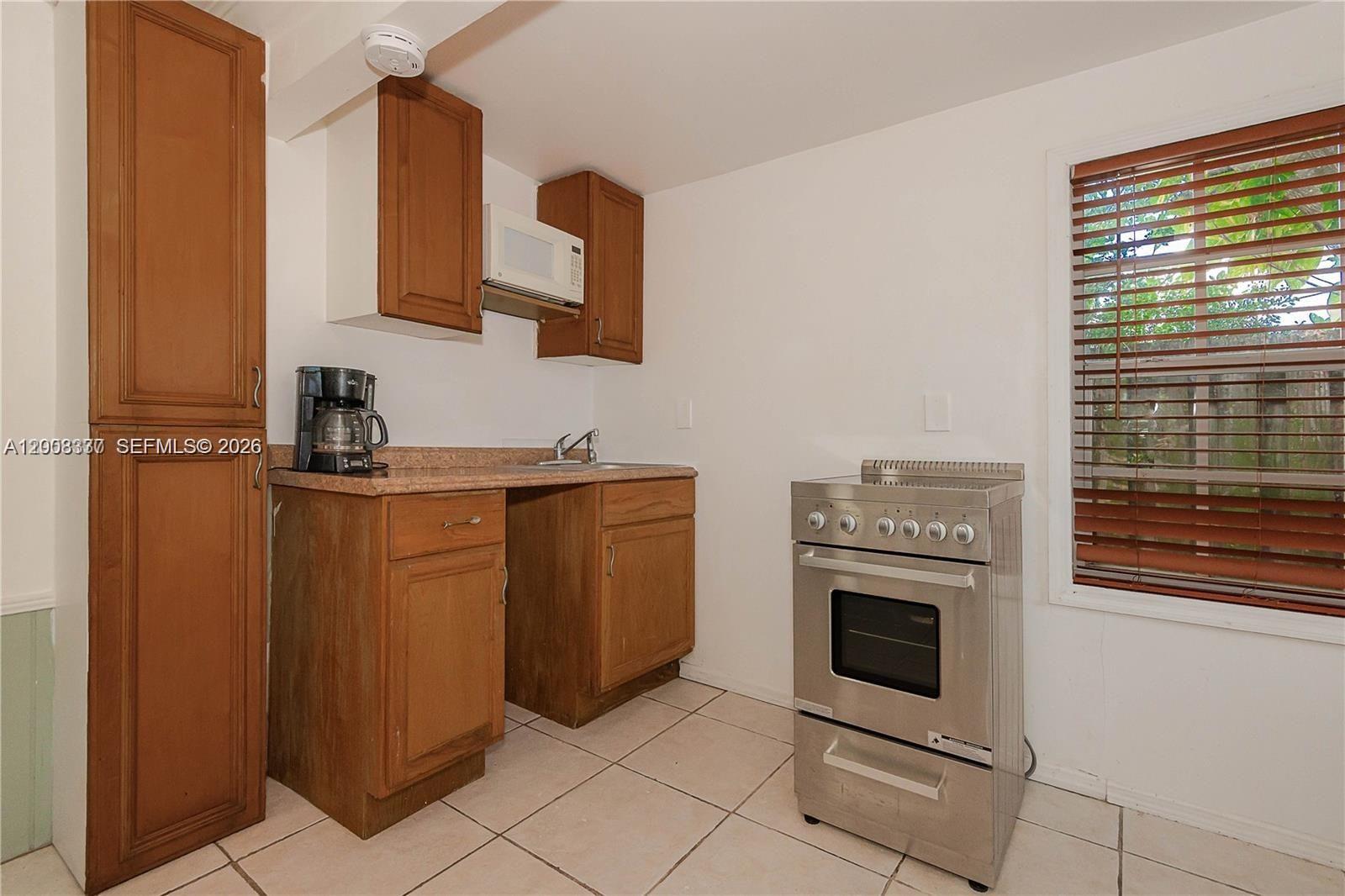 A small kitchen features wooden cabinets, a stainless steel stove, and a window with blinds — 1611 Fletcher St # 2, Hollywood FL 33020, HOLLYWOOD, FL