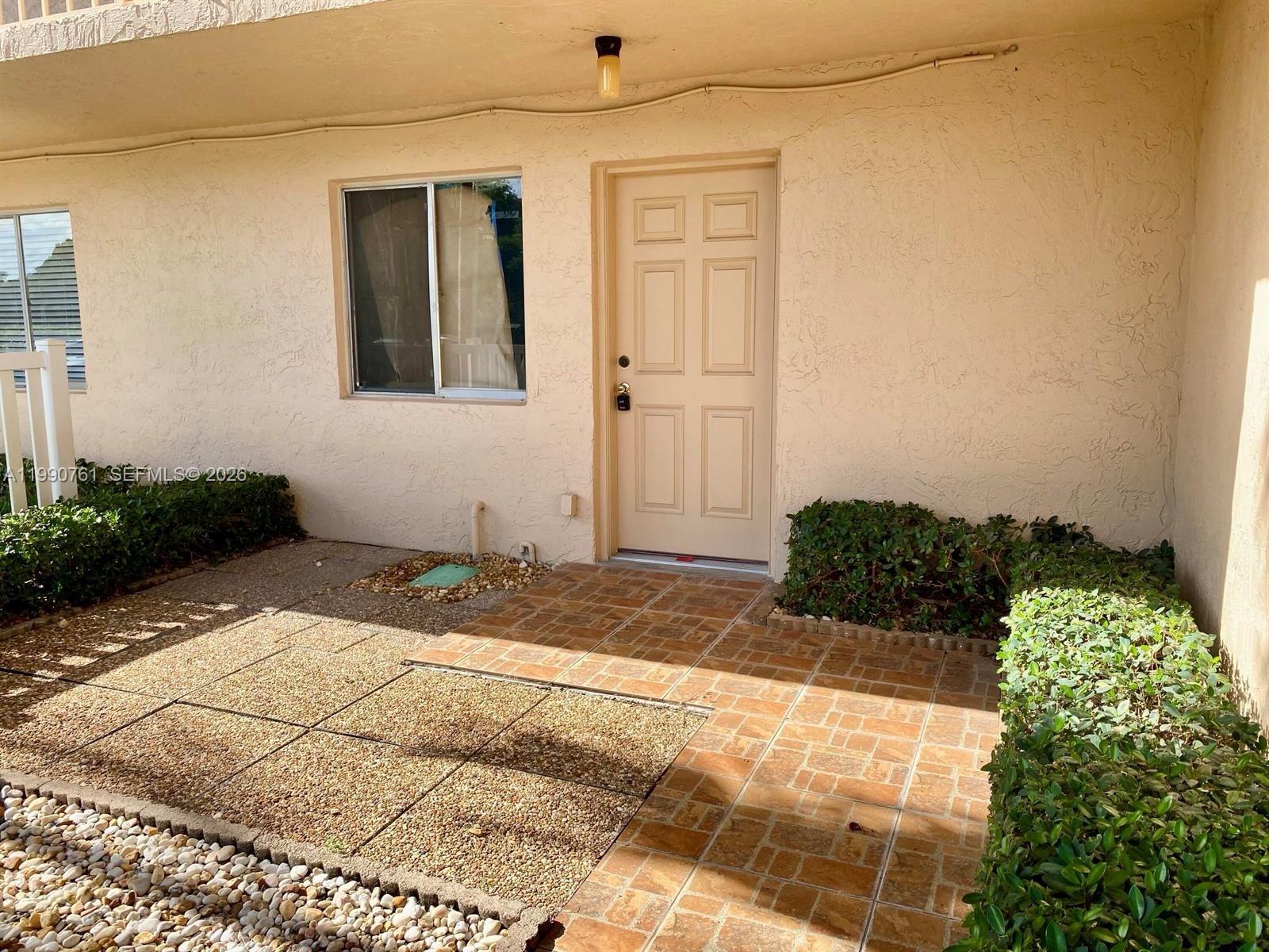 An exterior view shows a tan stucco building with a front door and tiled patio — 6935 Huntington Ln # 108, Delray Beach FL 33446, DELRAY BEACH, FL