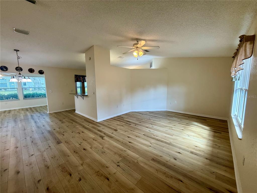 An open-concept living area features light wood-look flooring, a ceiling fan, and neutral walls — 8287 SW 116TH ST STREET, OCALA, FL