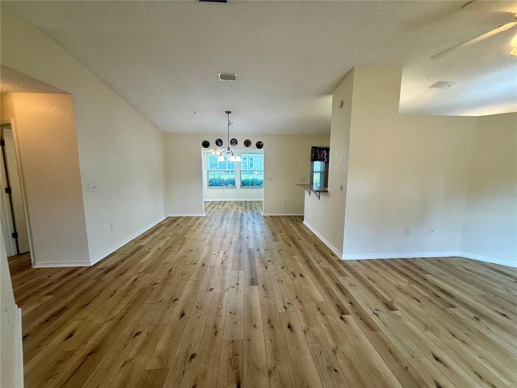 An open-concept living and dining area features light wood-look flooring and a vaulted ceiling — 8287 SW 116TH ST STREET, OCALA, FL