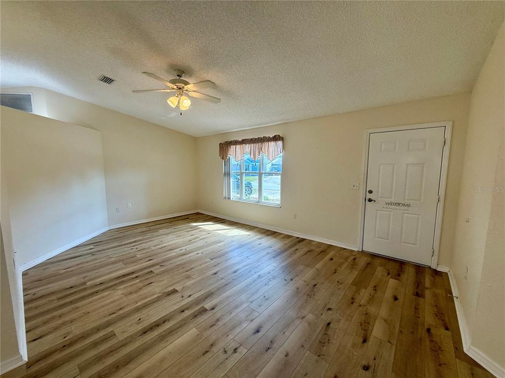 An empty living room features light wood-look flooring, a ceiling fan, and a front door — 8287 SW 116TH ST STREET, OCALA, FL