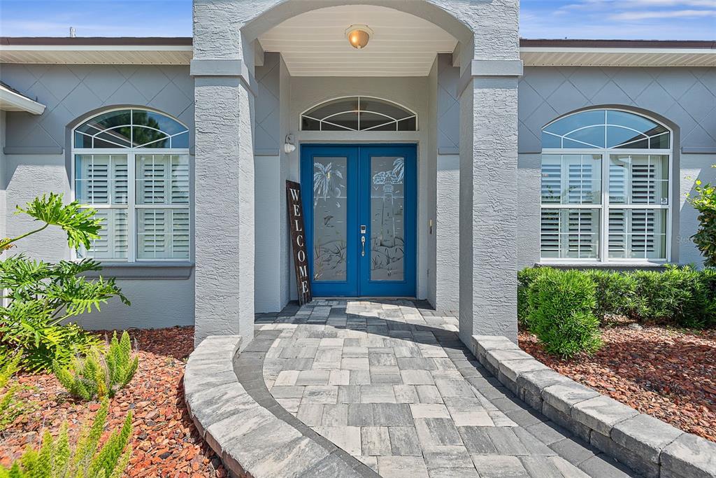 A paved walkway leads to a blue double front door with etched glass designs — 72 CLUB HOUSE DRIVE, PALM COAST, FL