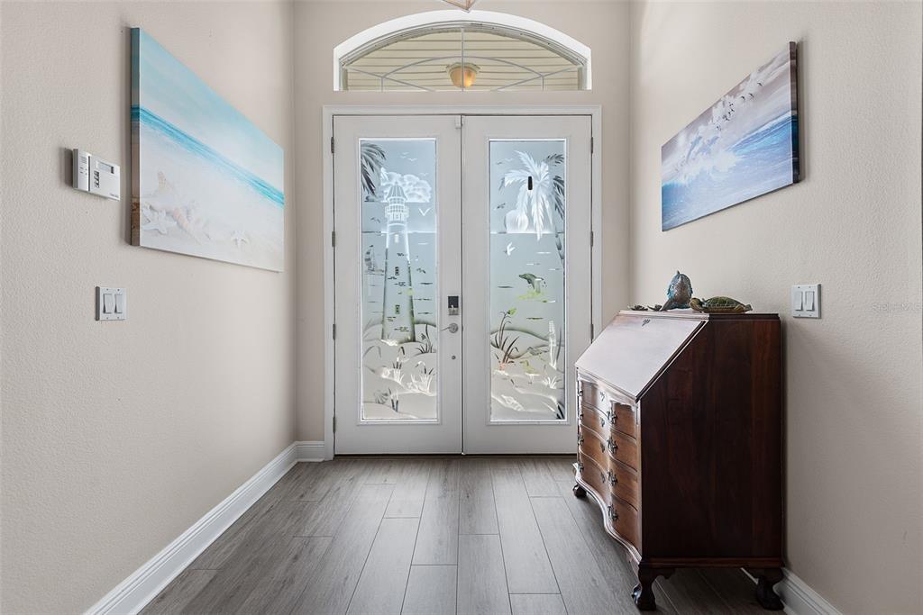 A foyer features a double door with etched glass, wood-look flooring, and coastal wall art — 72 CLUB HOUSE DRIVE, PALM COAST, FL