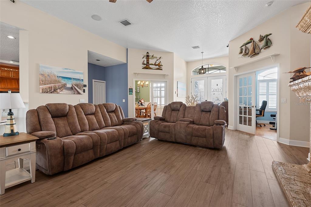 A living room features brown reclining sofas, wood-look flooring, and French doors leading outside — 72 CLUB HOUSE DRIVE, PALM COAST, FL