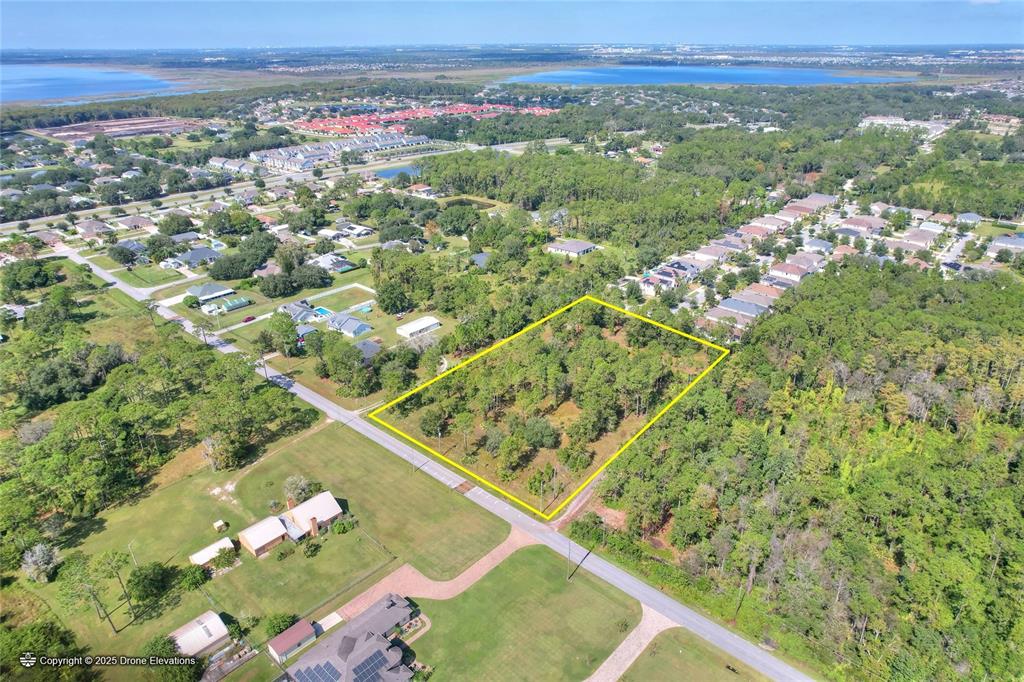 An aerial view shows a rectangular, tree-covered vacant lot outlined in yellow along a road — MOORE STREET, ST CLOUD, FL