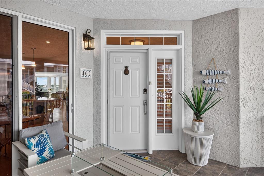 A covered balcony features tile flooring, a fire pit table, seating, and a tropical view — 1280 DOLPHIN BAY WAY UNIT 402, SARASOTA, FL