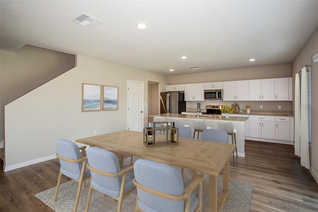 An open-concept kitchen and dining area features light wood floors, white cabinetry, and blue chairs — 36690 THORNHEDGE DRIVE, ZEPHYRHILLS, FL