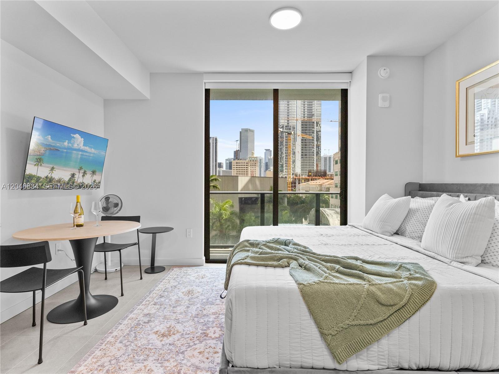 A bedroom features a bed, a small dining table, and a balcony with city views — 121 NE 5th St # 504, Miami FL 33132, MIAMI, FL