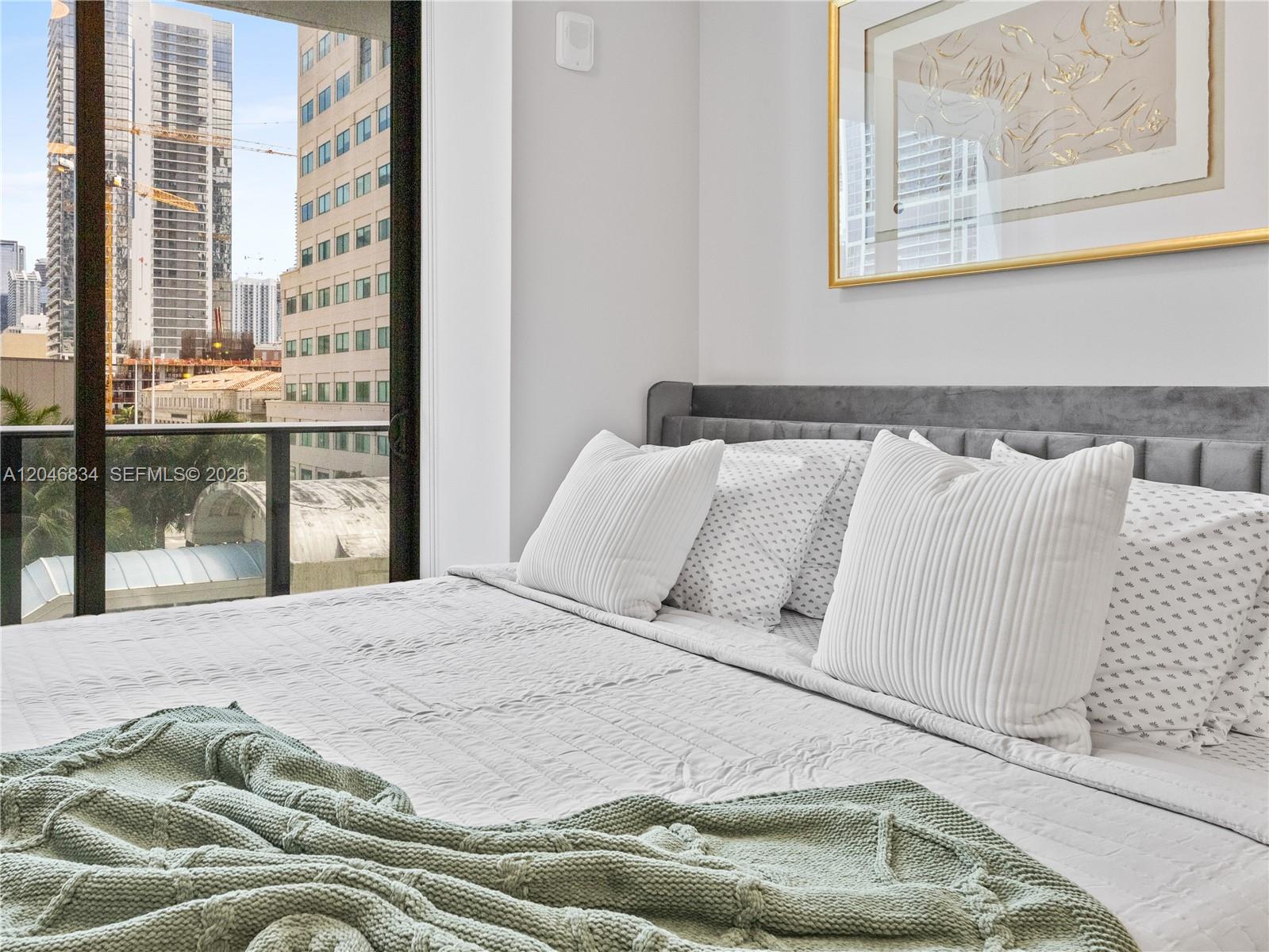 A bedroom features a gray upholstered headboard, white bedding, and a view of city buildings — 121 NE 5th St # 504, Miami FL 33132, MIAMI, FL