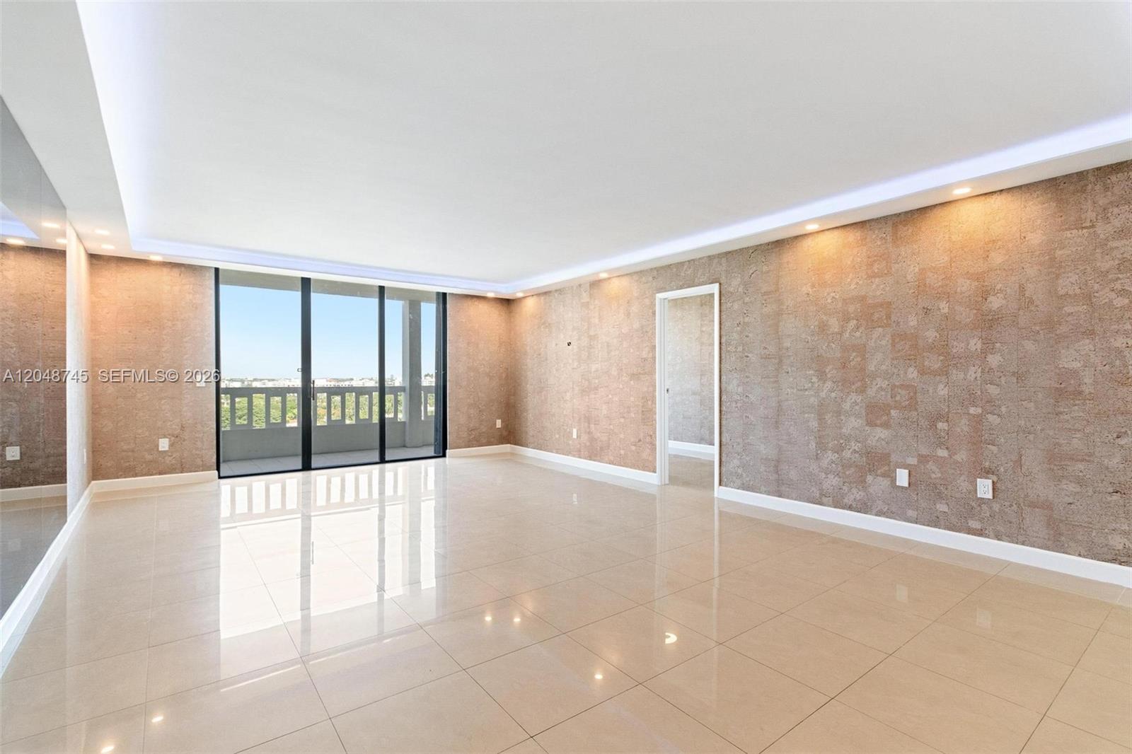 An empty room features glossy tile floors, textured accent walls, and a large sliding glass door — 9801 Collins Ave # O, Bal Harbour FL 33154, BAL HARBOUR, FL