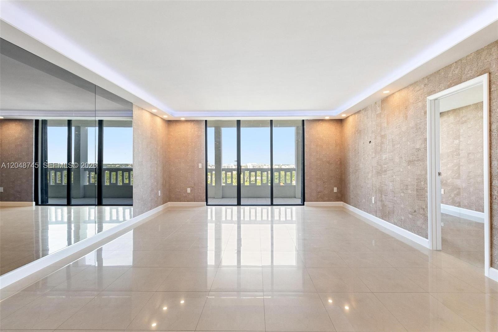 A bright, empty room features polished tile floors, textured walls, and large glass balcony doors — 9801 Collins Ave # O, Bal Harbour FL 33154, BAL HARBOUR, FL