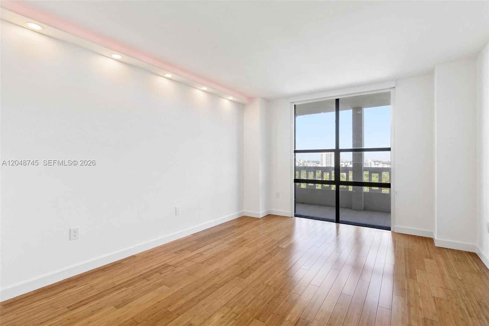 An empty room features light wood flooring, white walls, recessed lighting, and a glass balcony door — 9801 Collins Ave # O, Bal Harbour FL 33154, BAL HARBOUR, FL