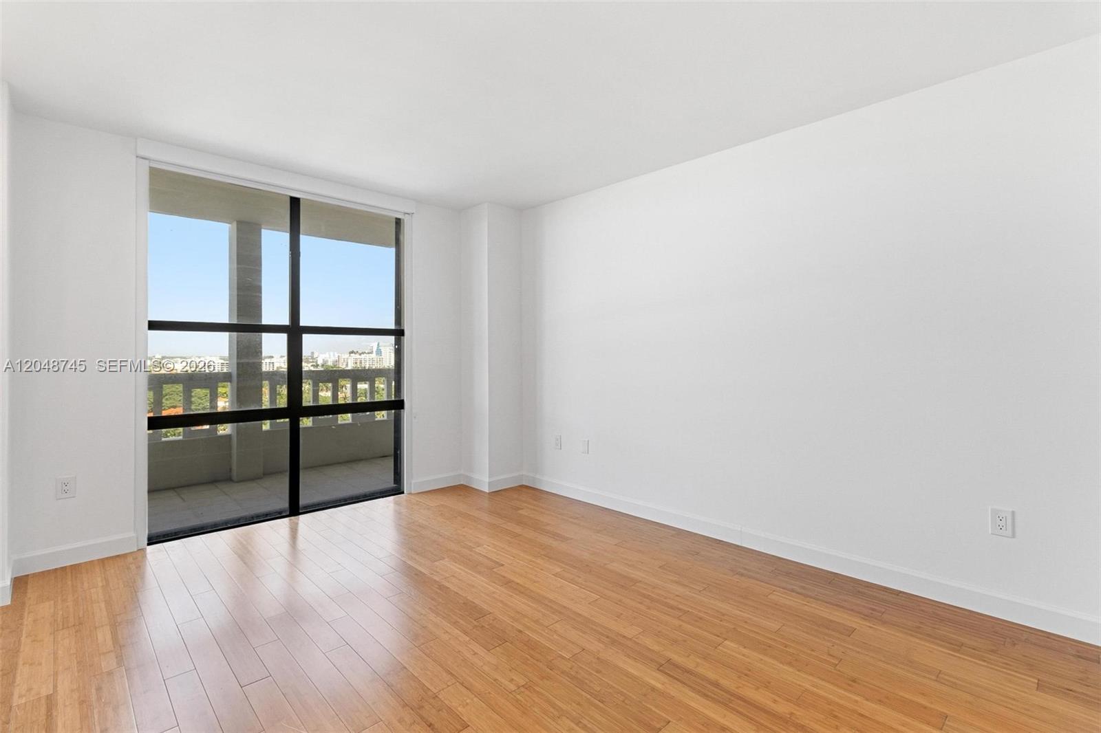 An empty room features light wood flooring, white walls, and a large sliding glass door — 9801 Collins Ave # O, Bal Harbour FL 33154, BAL HARBOUR, FL
