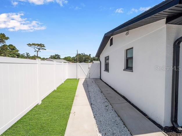 A white house exterior features a side walkway with gravel, a lawn, and a fence — 6040 84TH AVENUE N, PINELLAS PARK, FL