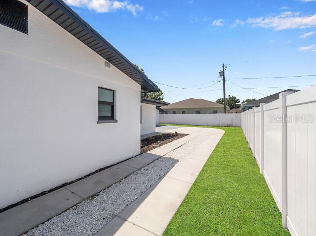 A white house exterior features a concrete walkway, gravel strip, and a white vinyl fence — 6040 84TH AVENUE N, PINELLAS PARK, FL