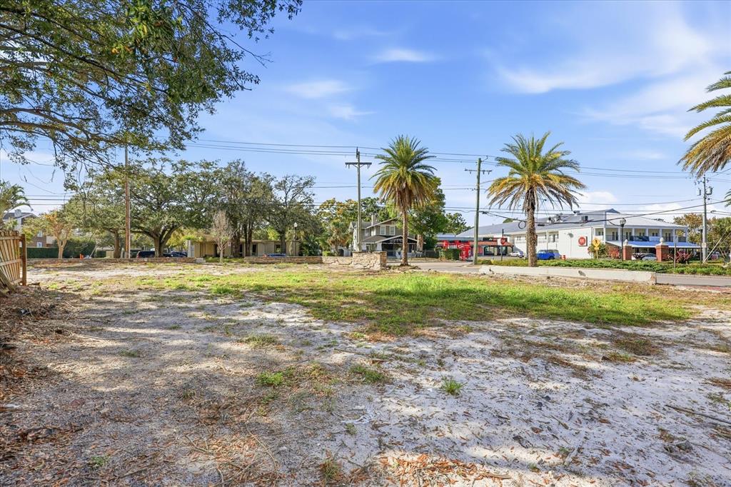 A vacant, sandy lot features scattered patches of grass, palm trees, and surrounding buildings — 1504 S HOWARD AVENUE, TAMPA, FL