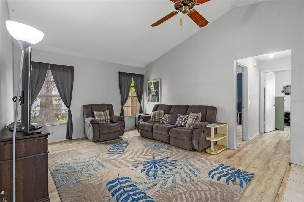 A living room features a vaulted ceiling, wood-look flooring, a sofa, and a recliner — 14058 SULLIVAN STREET, SPRING HILL, FL