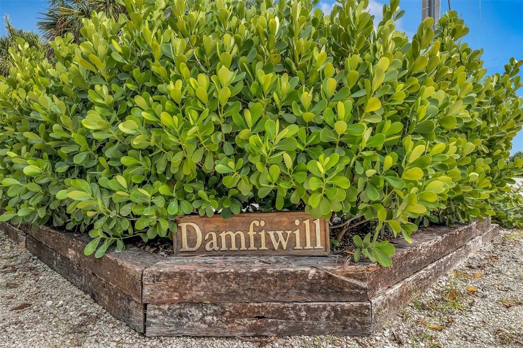 A wooden sign reading Damfiwill sits in front of a large green shrub in a garden — 171 DAMFIWILL STREET, BOCA GRANDE, FL