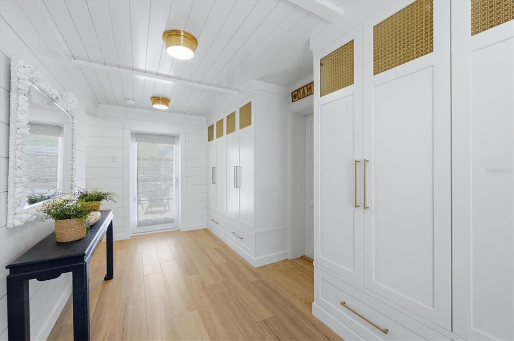 A bright hallway features white shiplap walls, built-in cabinetry with gold accents, and wood flooring — 171 DAMFIWILL STREET, BOCA GRANDE, FL