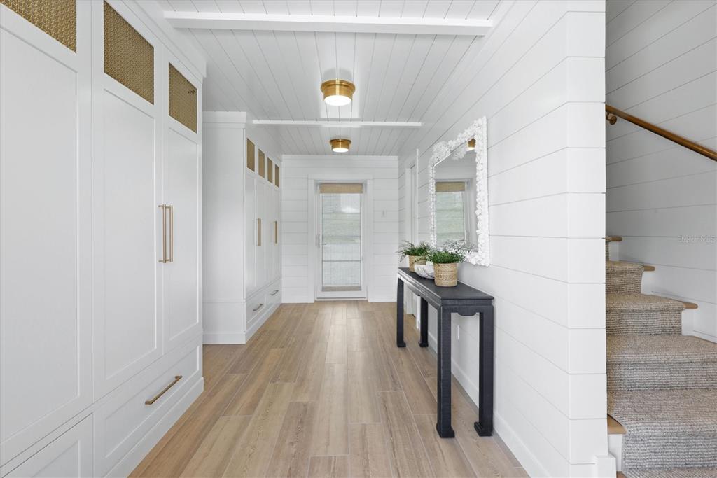 A bright hallway features white shiplap walls, built-in cabinetry, a black console table, and stairs — 171 DAMFIWILL STREET, BOCA GRANDE, FL