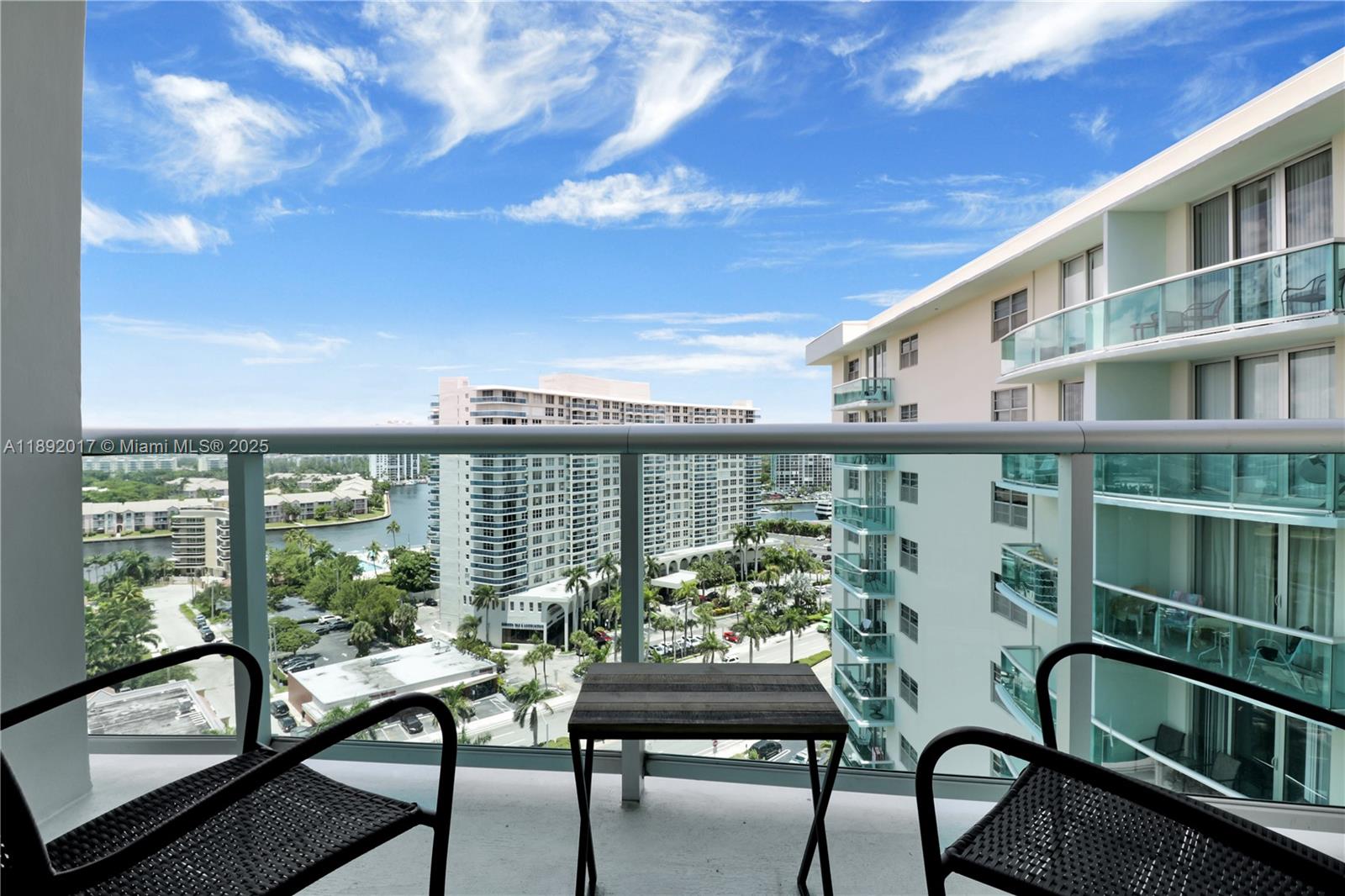 A balcony view features two chairs, a small table, and a cityscape with water — 3901 S Ocean Dr # 15R, Hollywood FL 33019, HOLLYWOOD, FL