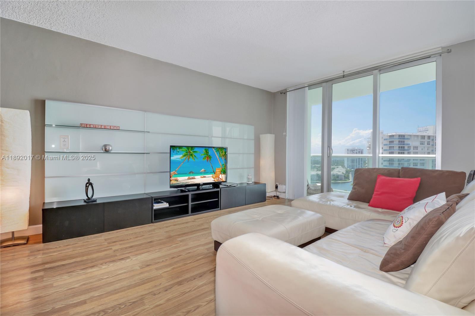 A living room features a white media wall, a white sectional sofa, and floor-to-ceiling windows — 3901 S Ocean Dr # 15R, Hollywood FL 33019, HOLLYWOOD, FL