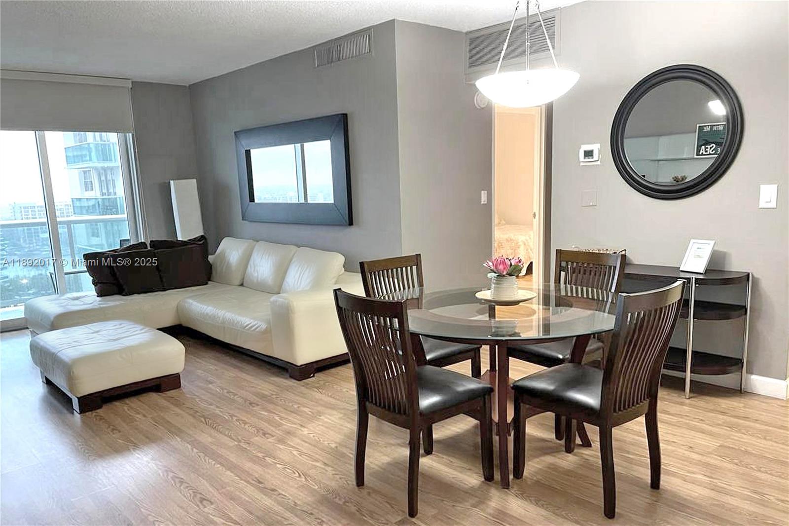 A living and dining area features a white sectional sofa, glass-topped table, and wood flooring — 3901 S Ocean Dr # 15R, Hollywood FL 33019, HOLLYWOOD, FL