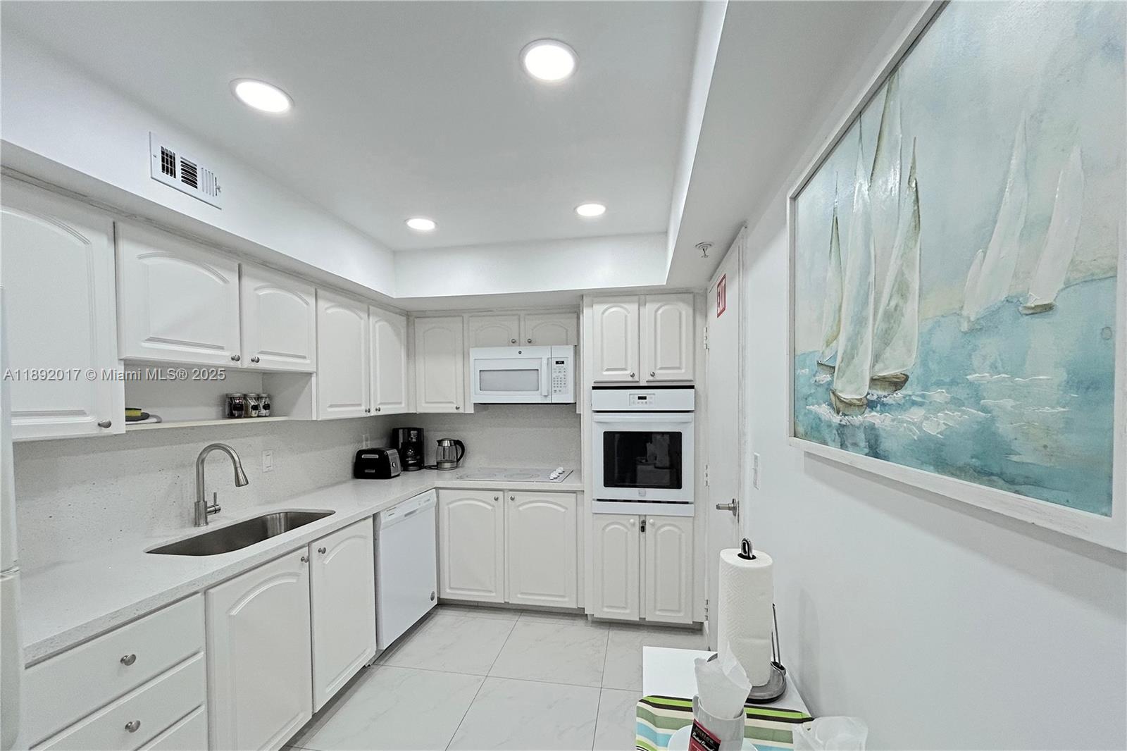 A white kitchen features cabinetry, a built-in oven, a microwave, and a sailboat painting — 3901 S Ocean Dr # 15R, Hollywood FL 33019, HOLLYWOOD, FL