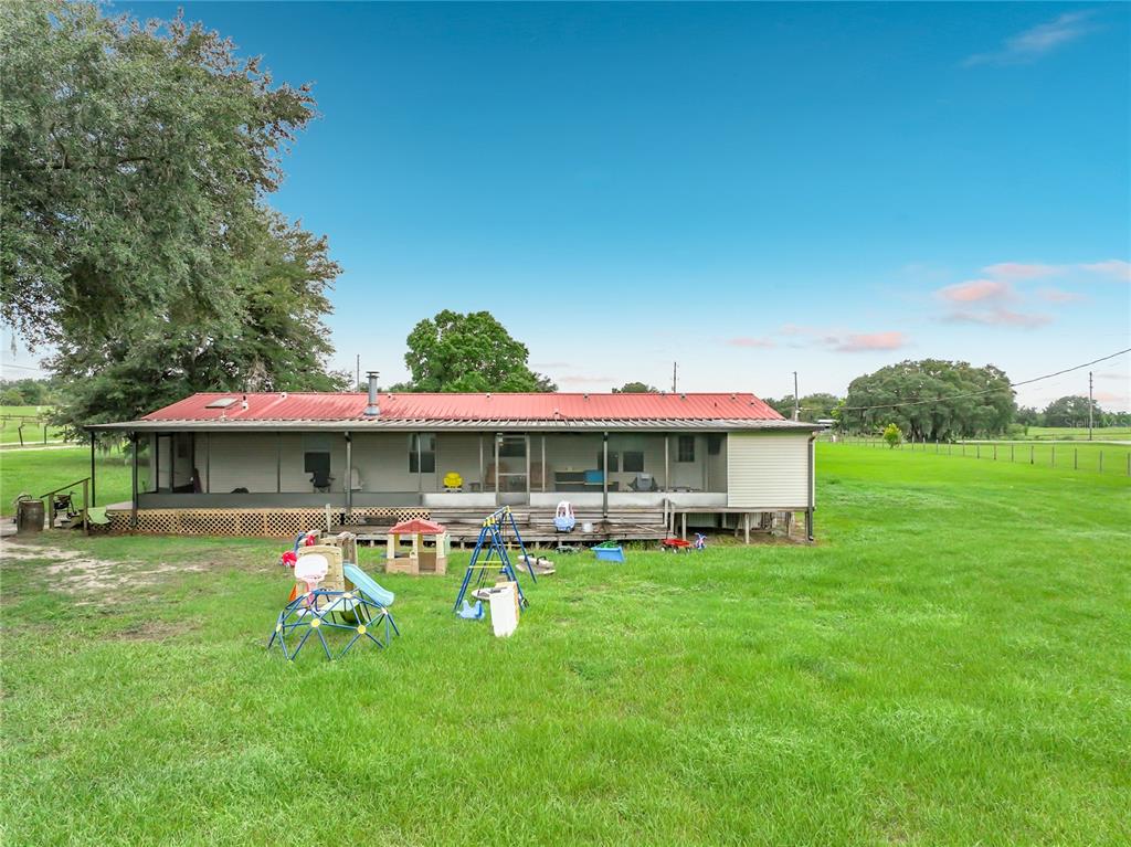 A single-story house with a red metal roof and a screened-in porch sits on grass — 23834 COUNTY ROAD 33, GROVELAND, FL