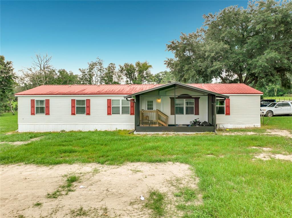 A single-story manufactured home with a red metal roof and a front screened-in porch — 23834 COUNTY ROAD 33, GROVELAND, FL