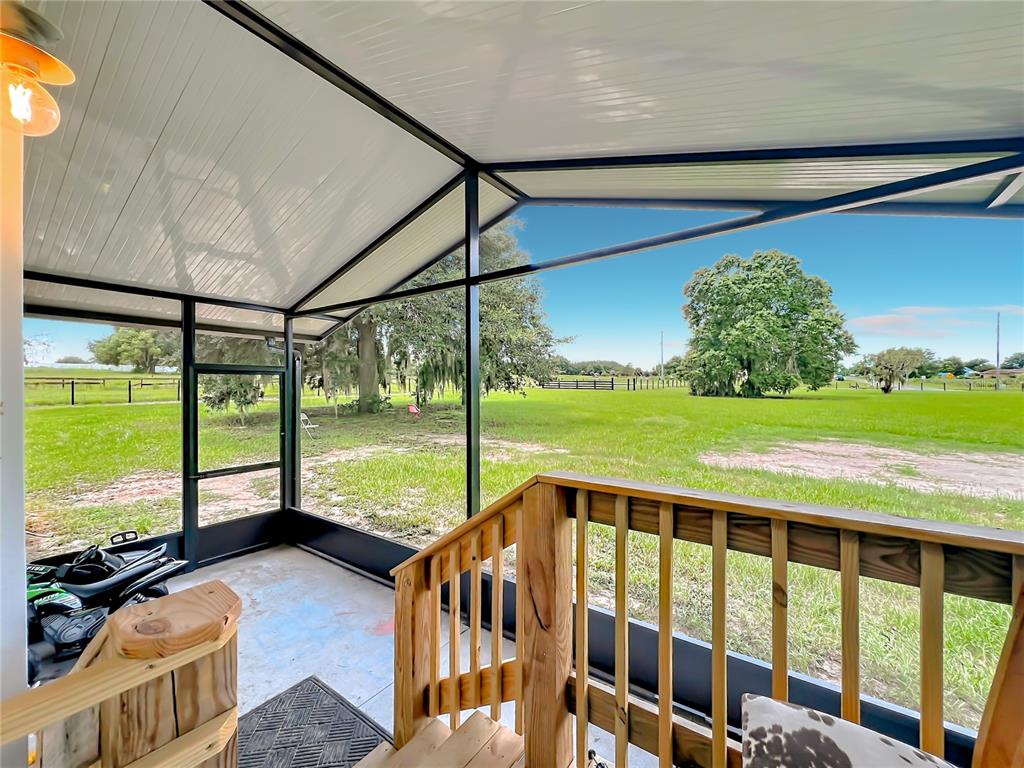 A screened-in porch with a wooden railing overlooks a large, grassy field with trees — 23834 COUNTY ROAD 33, GROVELAND, FL