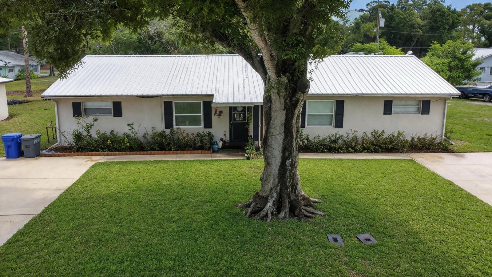 A single-story house with a white metal roof and a large tree in the yard — 1504 41st Avenue, Vero Beach FL 32960, VERO BEACH, FL