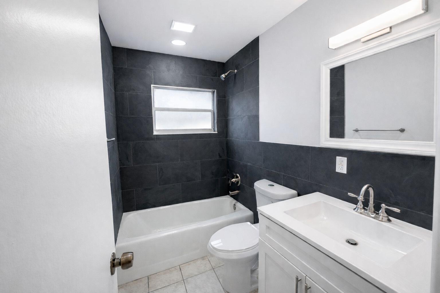 A bathroom with a white vanity, a toilet, and a bathtub with dark tile walls — 1504 41st Avenue, Vero Beach FL 32960, VERO BEACH, FL
