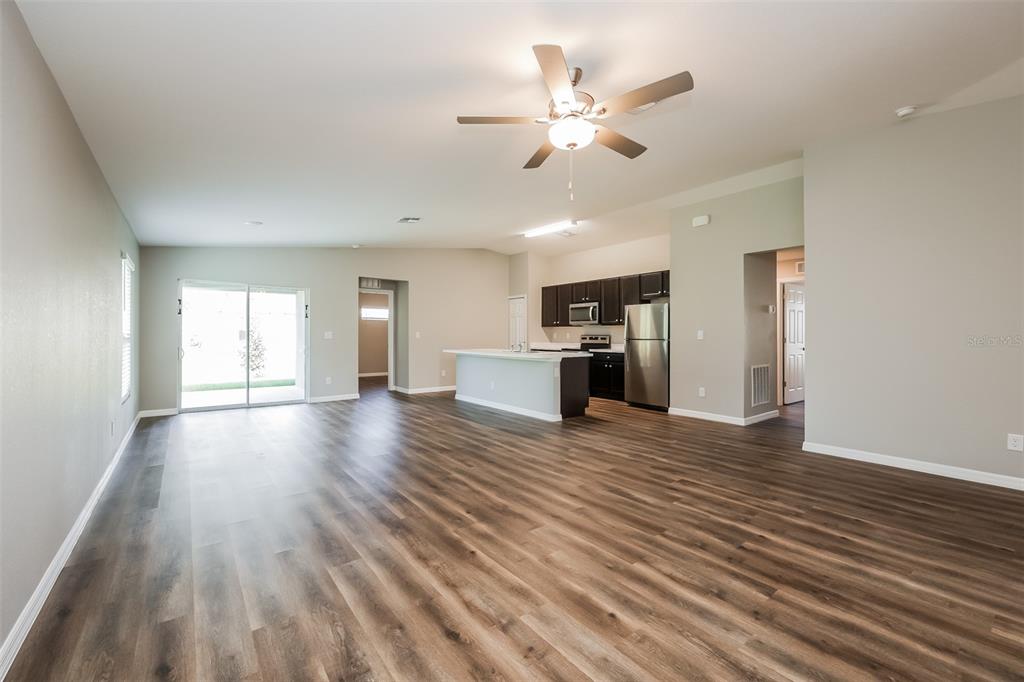 An open-concept living area features wood-look flooring, a ceiling fan, and an adjacent kitchen — 4458 WINDSONG AVENUE, NORTH PORT, FL