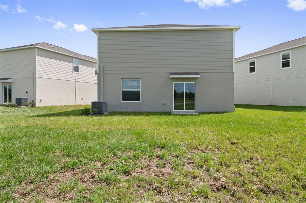 The rear exterior of a two-story house features a sliding glass door and a window — 11709 NOBLE BLOSSOM LOOP, DADE CITY, FL