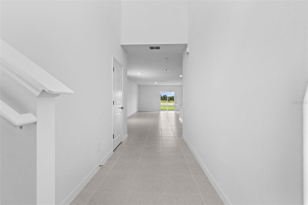 A bright hallway with light tile flooring leads toward a glass door at the back — 11709 NOBLE BLOSSOM LOOP, DADE CITY, FL