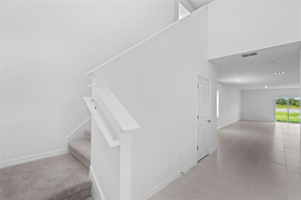 An interior view showing a carpeted staircase next to a white door and tiled hallway — 11709 NOBLE BLOSSOM LOOP, DADE CITY, FL