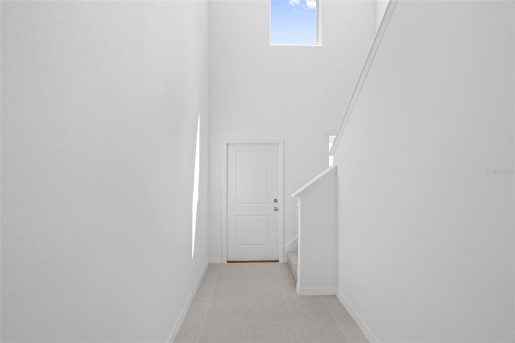 A bright entryway with white walls, tile flooring, a front door, and a staircase — 11709 NOBLE BLOSSOM LOOP, DADE CITY, FL