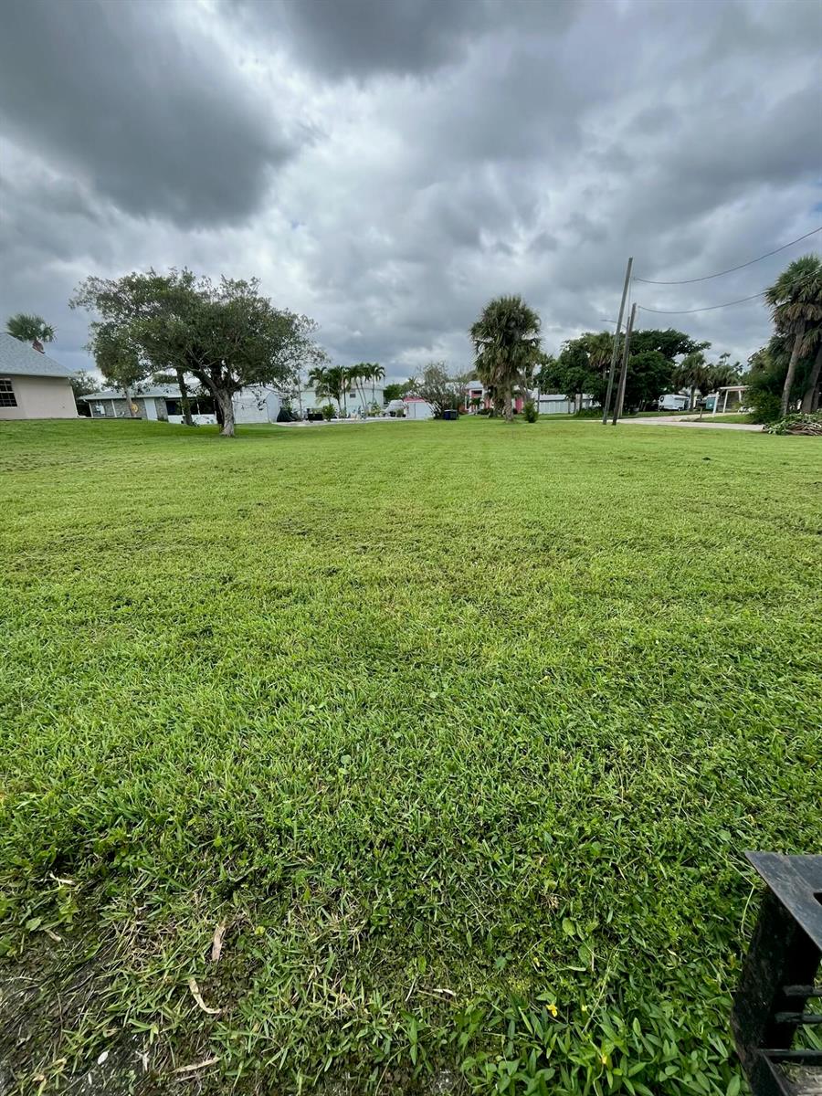 A large, flat, grassy residential lot under a cloudy sky with surrounding trees and houses — 0 Coral Circle, Fort Pierce FL 34949, FORT PIERCE, FL