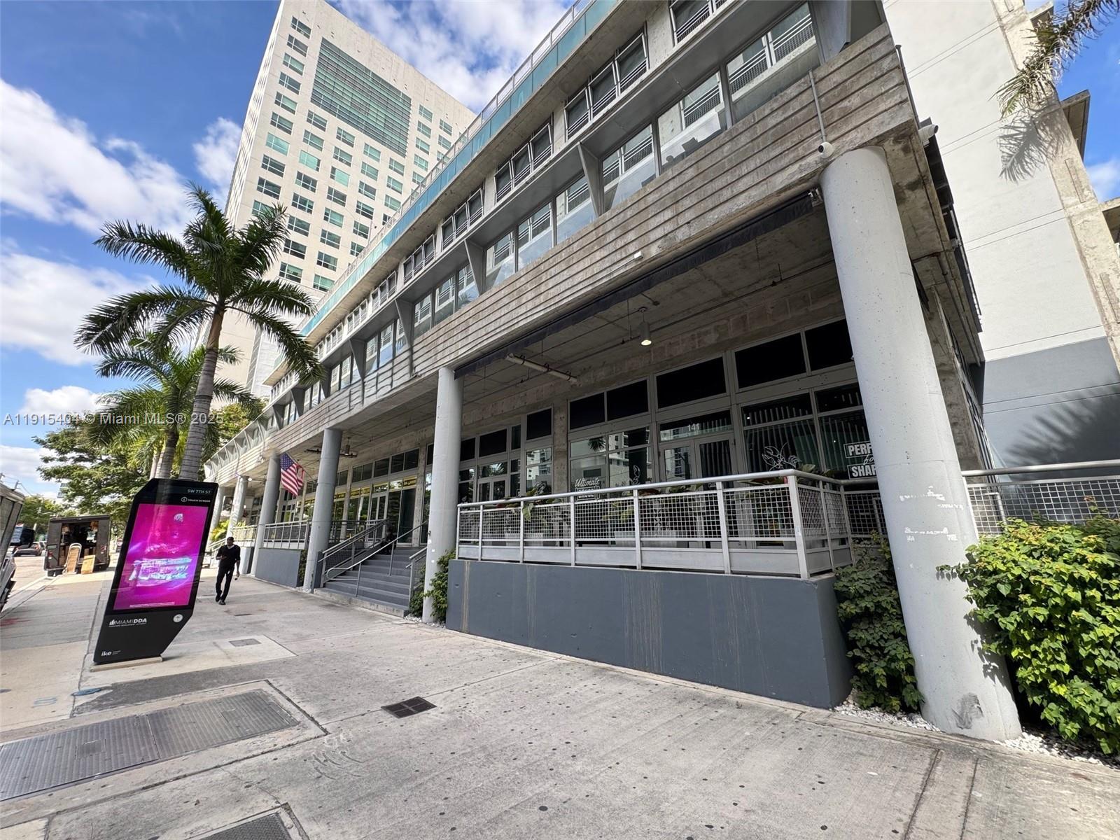 A modern multi-story building with a concrete facade, glass windows, and a street-level patio — 169 SW 7th St # D, Miami FL 33130, MIAMI, FL