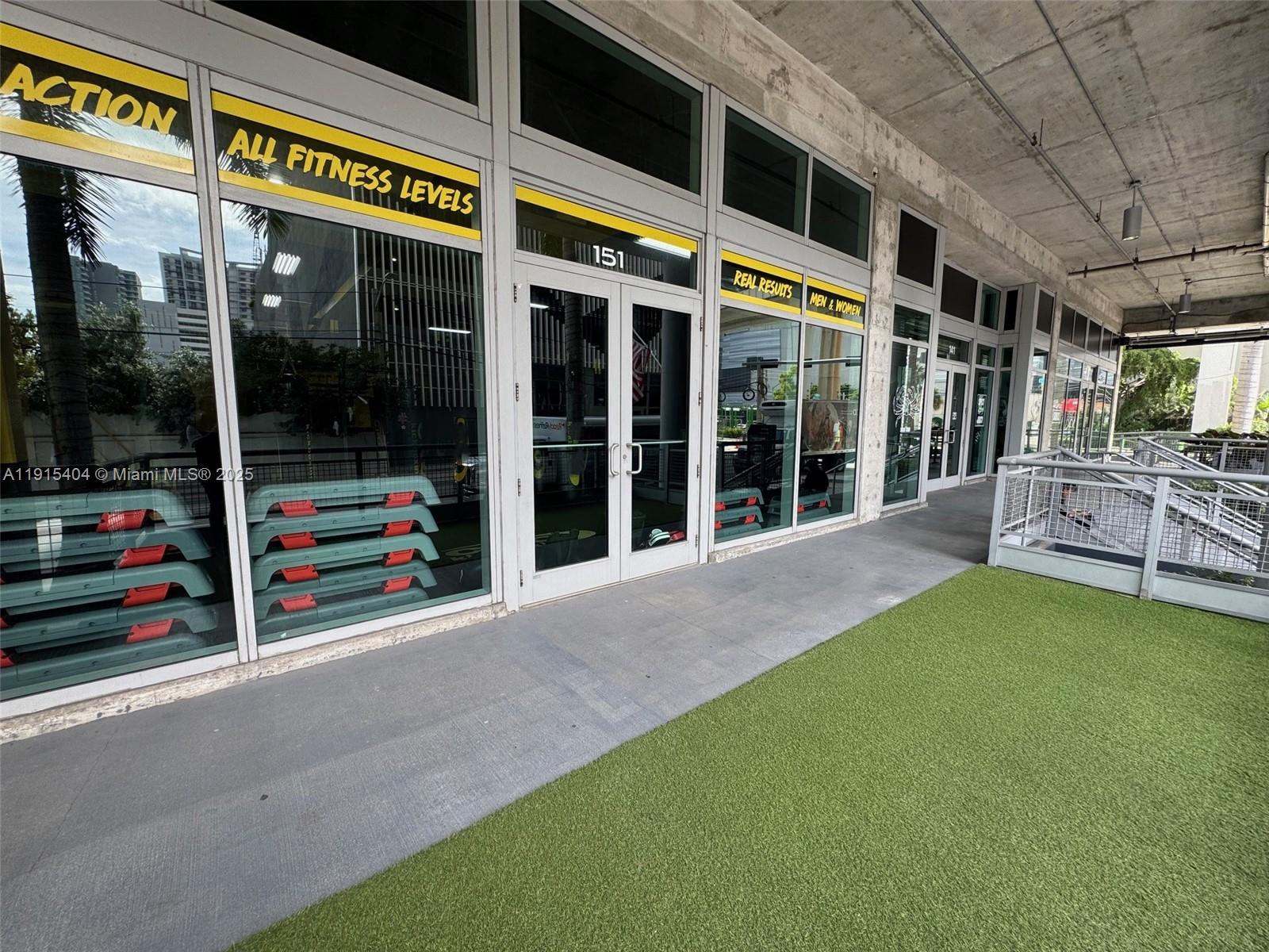 The exterior of a fitness center features glass storefronts, a concrete ceiling, and artificial turf — 169 SW 7th St # D, Miami FL 33130, MIAMI, FL