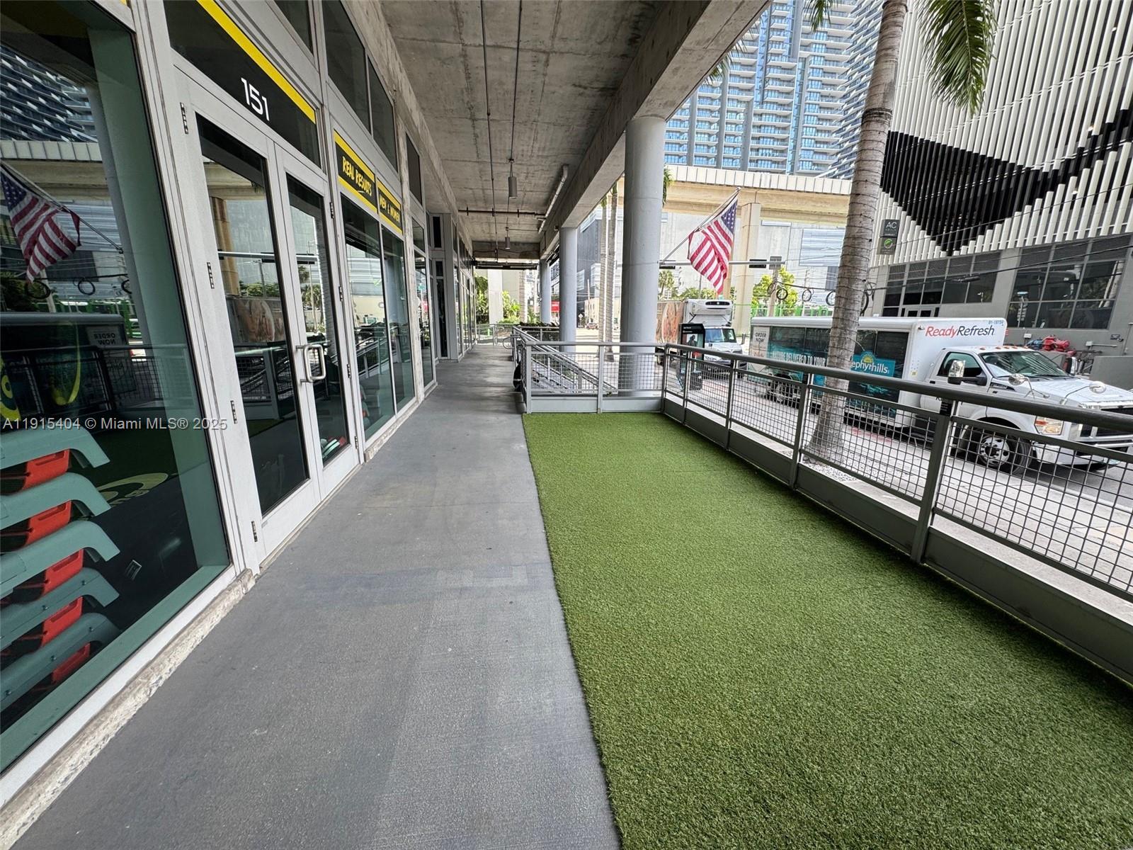 A concrete walkway features a section of artificial turf alongside a building with glass doors — 169 SW 7th St # D, Miami FL 33130, MIAMI, FL