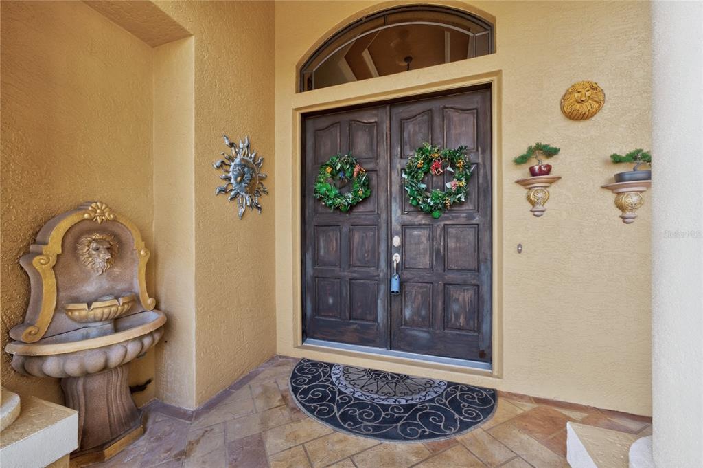 An exterior entryway features double wooden doors, a stone fountain, and decorative wall accents — 1141 ROTONDA CIRCLE, ROTONDA WEST, FL