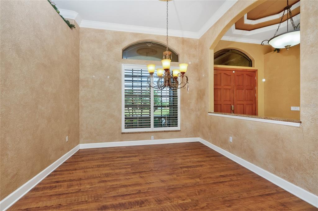 A dining room with wood-look flooring, textured beige walls, a chandelier, and plantation shutters — 1141 ROTONDA CIRCLE, ROTONDA WEST, FL
