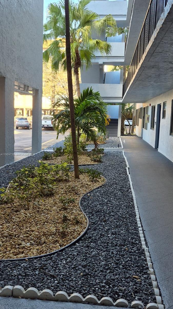 A walkway runs alongside a landscaped garden bed with palm trees and decorative gravel — 8020 Hampton Blvd # 202, North Lauderdale FL 33068, NORTH LAUDERDALE, FL