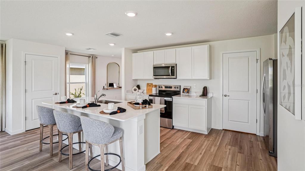 A modern kitchen features a white island with bar stools, stainless steel appliances, and wood-look flooring — 9062 SW 47TH COURT, OCALA, FL