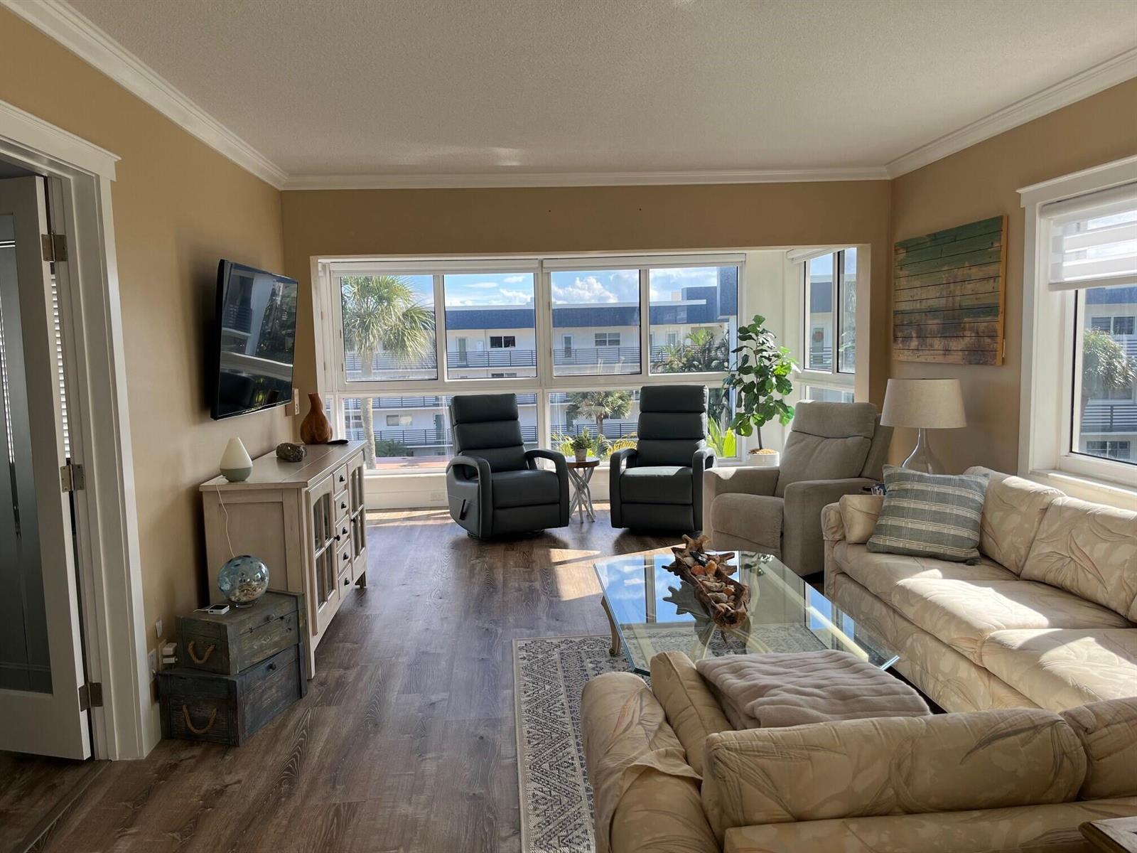 A living room features a glass coffee table, two dark recliners, and large windows — 3401 Spanish Trail # 455, Delray Beach FL 33483, DELRAY BEACH, FL