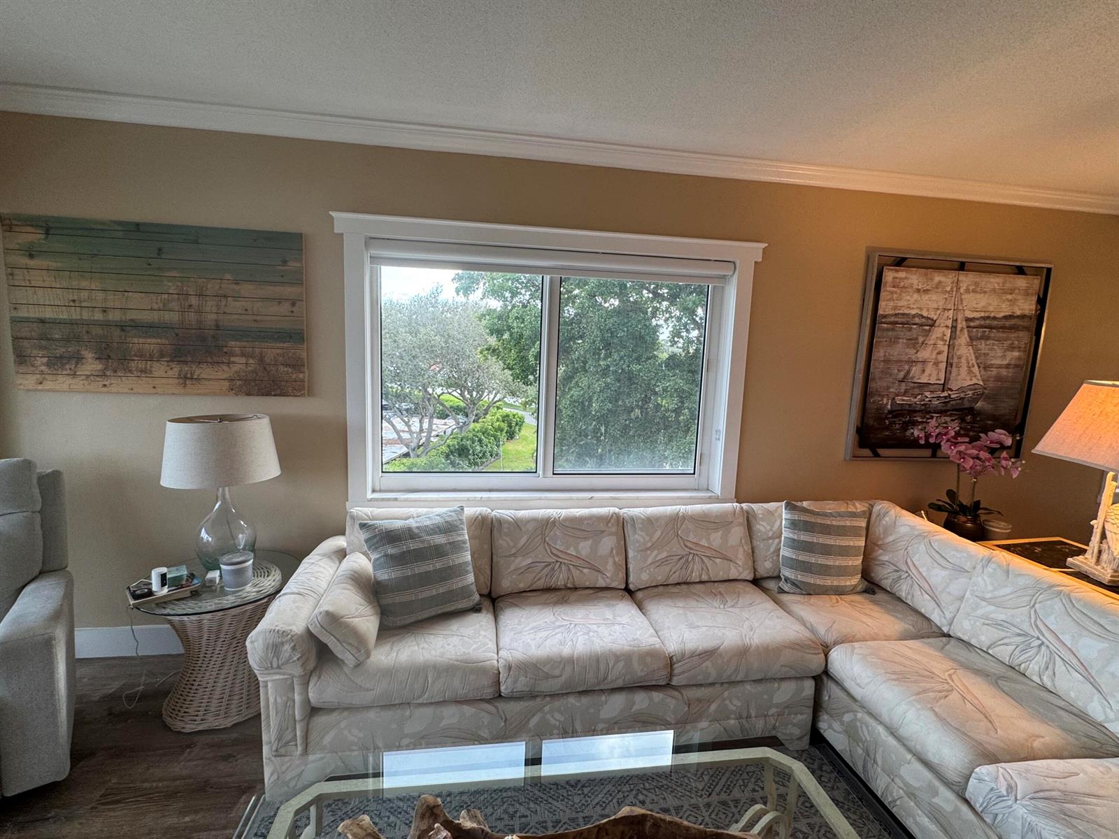 A living room features a beige sectional sofa, a window with a view, and wall art — 3401 Spanish Trail # 455, Delray Beach FL 33483, DELRAY BEACH, FL