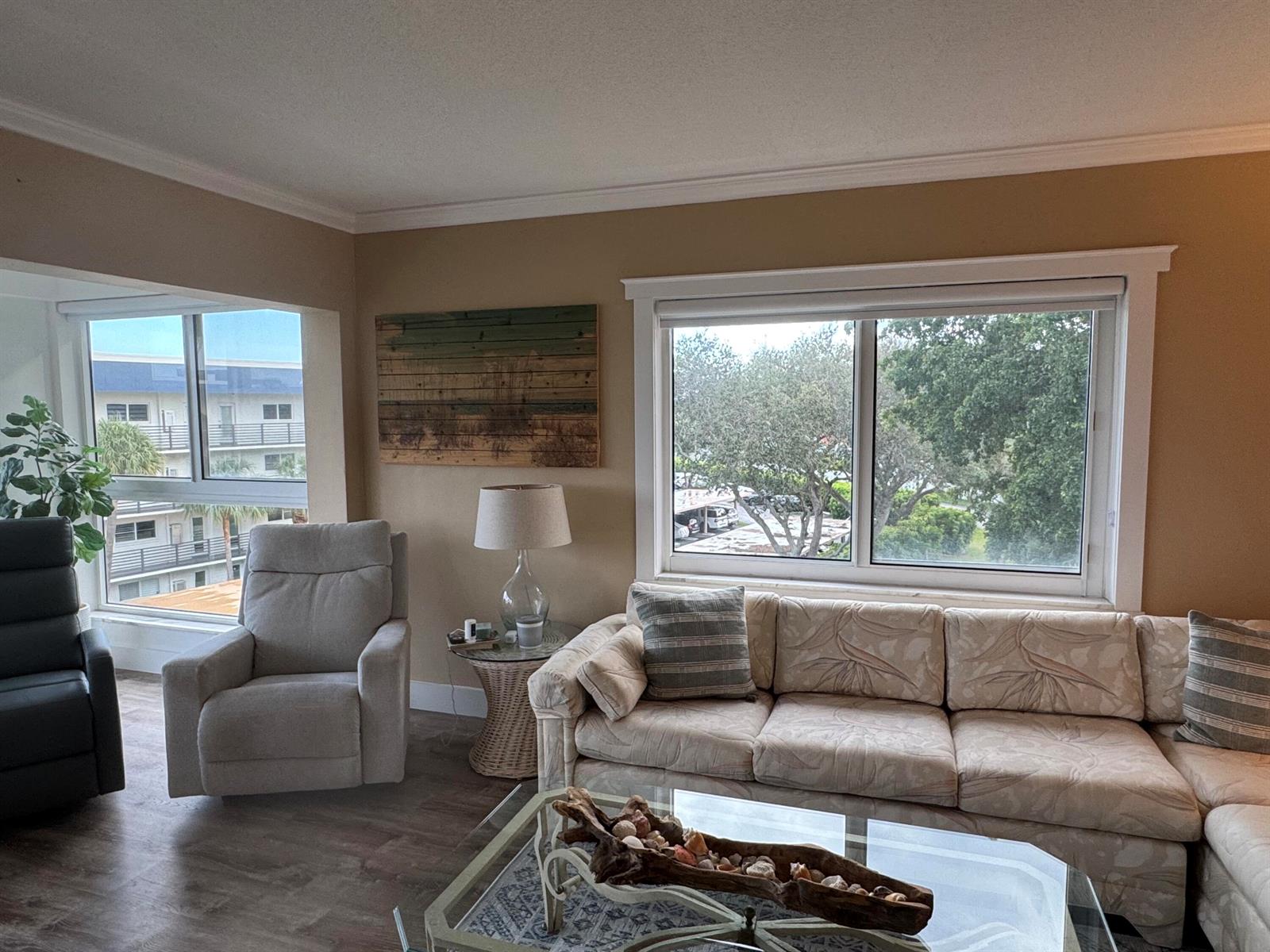 A living room features a beige sofa, a recliner, and a large window overlooking trees — 3401 Spanish Trail # 455, Delray Beach FL 33483, DELRAY BEACH, FL