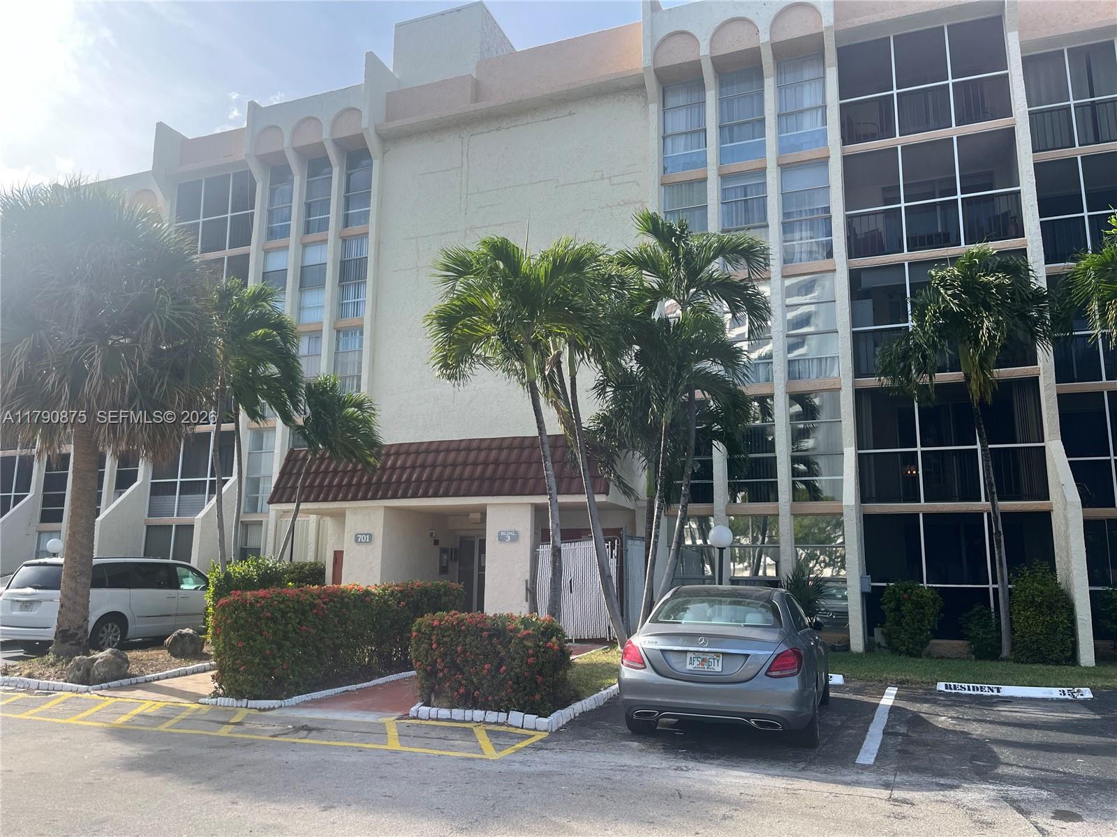 A multi-story apartment building exterior features palm trees, a parking lot, and a covered entrance — 701 Three Islands Blvd # 409, Hallandale Beach FL 33009, HALLANDALE BEACH, FL